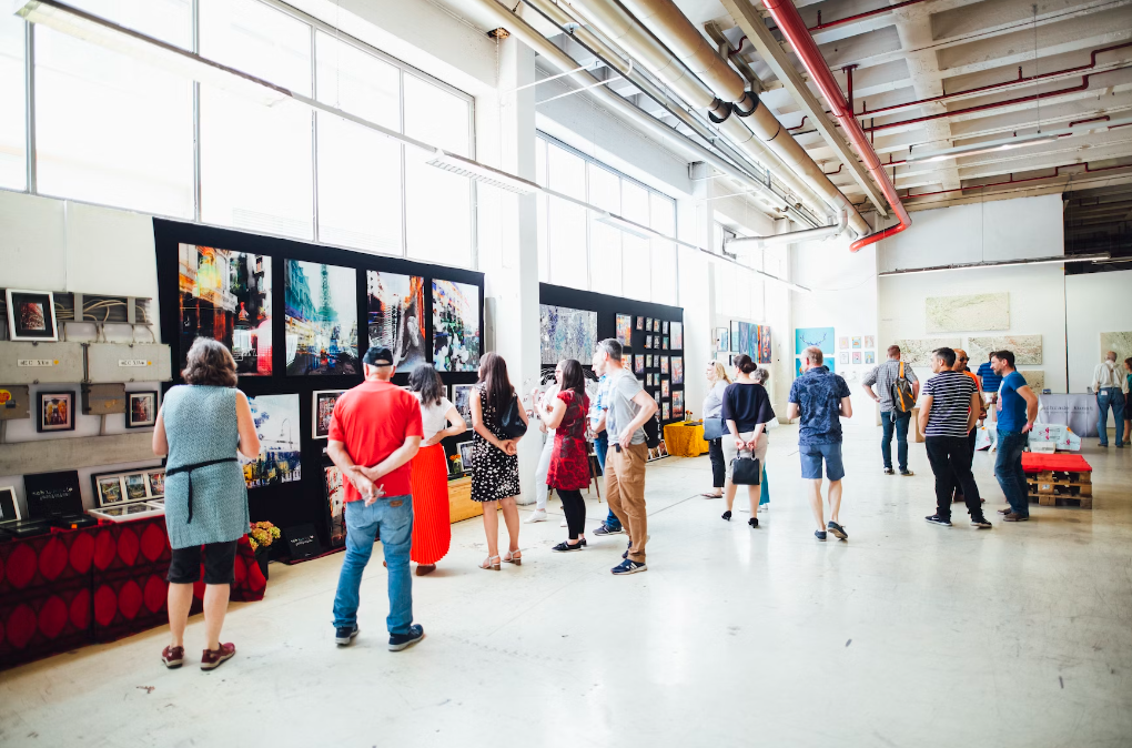 a wide shot of a brightly lit gallery exhibition with several people looking at large, colorful prints